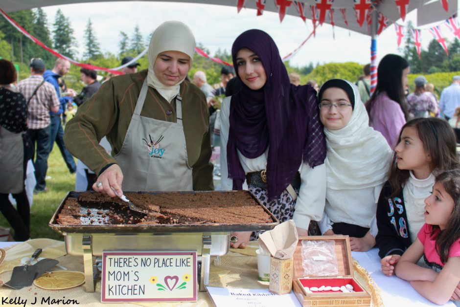 A multi-generational family of women in hijabs serve food to guests.
