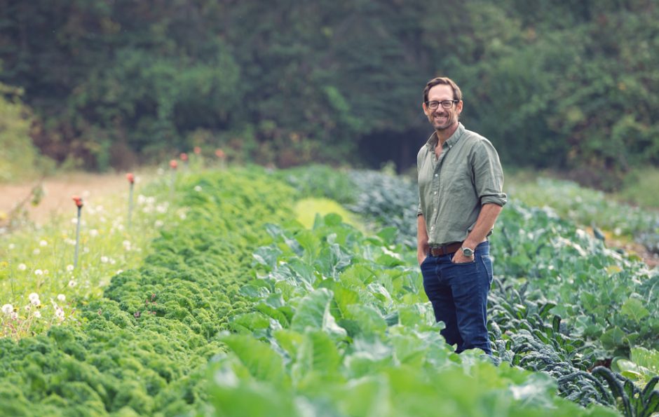 Sean Smukler standing in a green farm field of kale, at the UBC Farm.