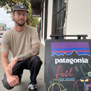 Zac Elik, manager of Patagonia's Vancouver store crouching in front of a Patagonia sign