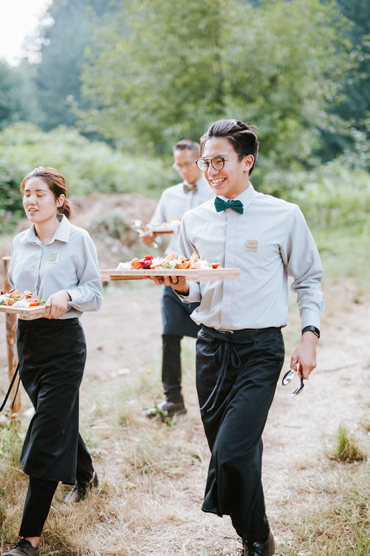 Servers bringing in dishes of food through a UBC Farm field.